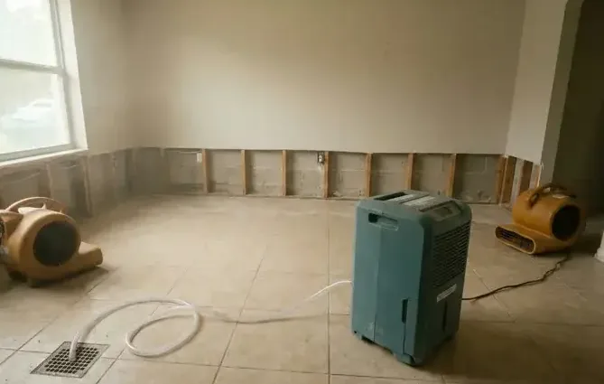 Dehumidifier and air movers running in a room with the baseboards pulled off for drying
