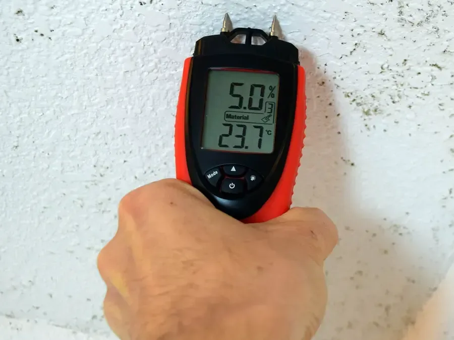 A moisture meter pressed to a wall to check how wet the drywall still is