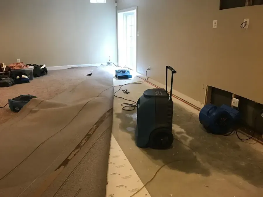 A dehumidifier and air mover running beside carpet pulled back from the floor