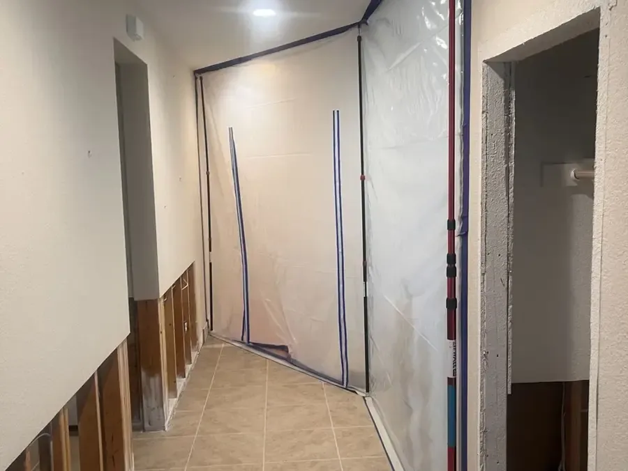 Hallway sealed off with plastic containment and the lower drywall cut back so the wall cavities can dry