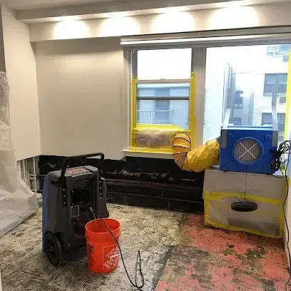 Dehumidifier and air mover running in a room stripped of flooring so the subfloor can dry out