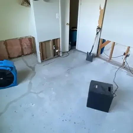 Air movers and a dehumidifier running in a room with the lower drywall cut away and the floor left bare