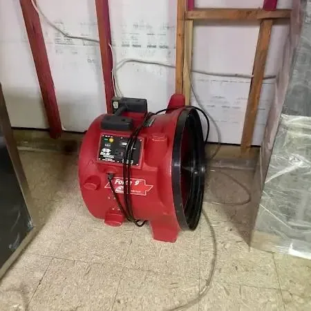 Red air mover drying a room with the lower wall opened and plastic sheeting hung to contain the wet area
