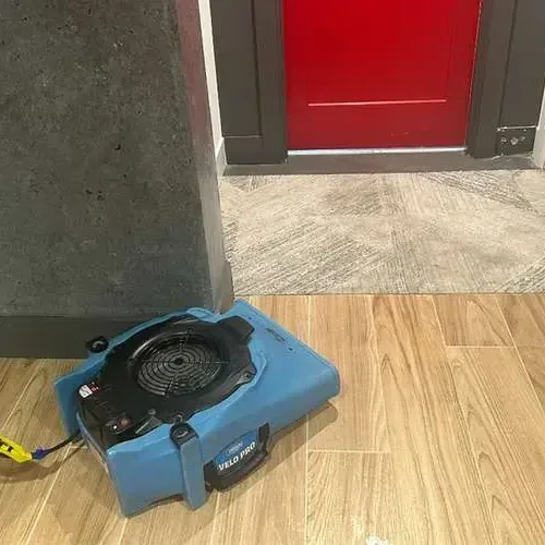 Air mover blowing across a wood look tile floor near an open doorway to dry the room