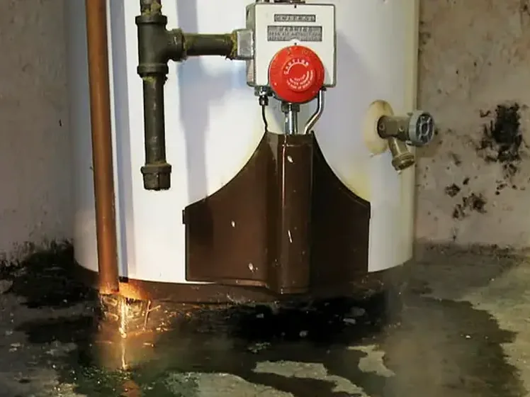 Leaking water heater tank pooling water across the floor around it